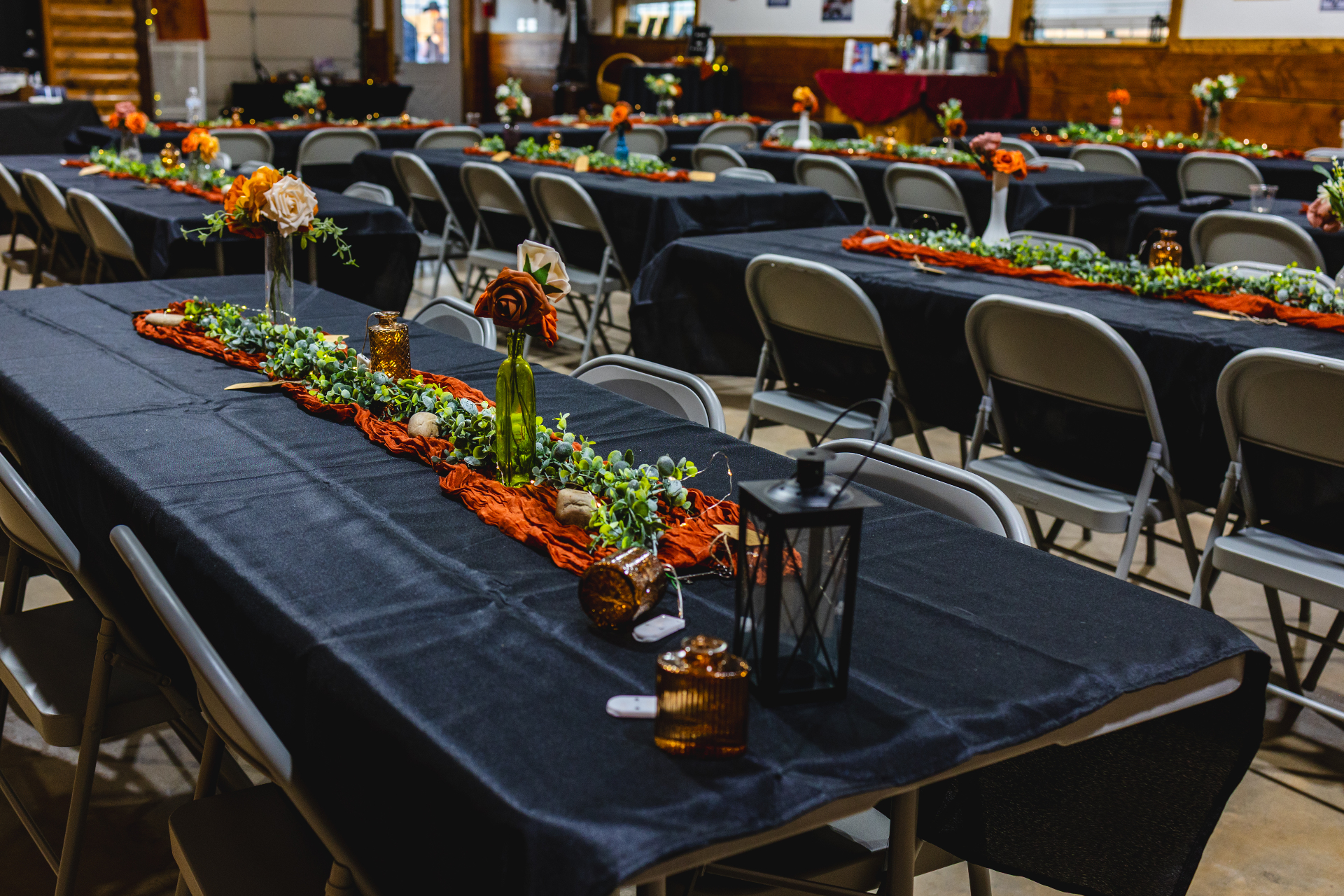 Reception hall with long black-linen tables, terracotta runners, eucalyptus garlands, amber lanterns, and rose centerpieces