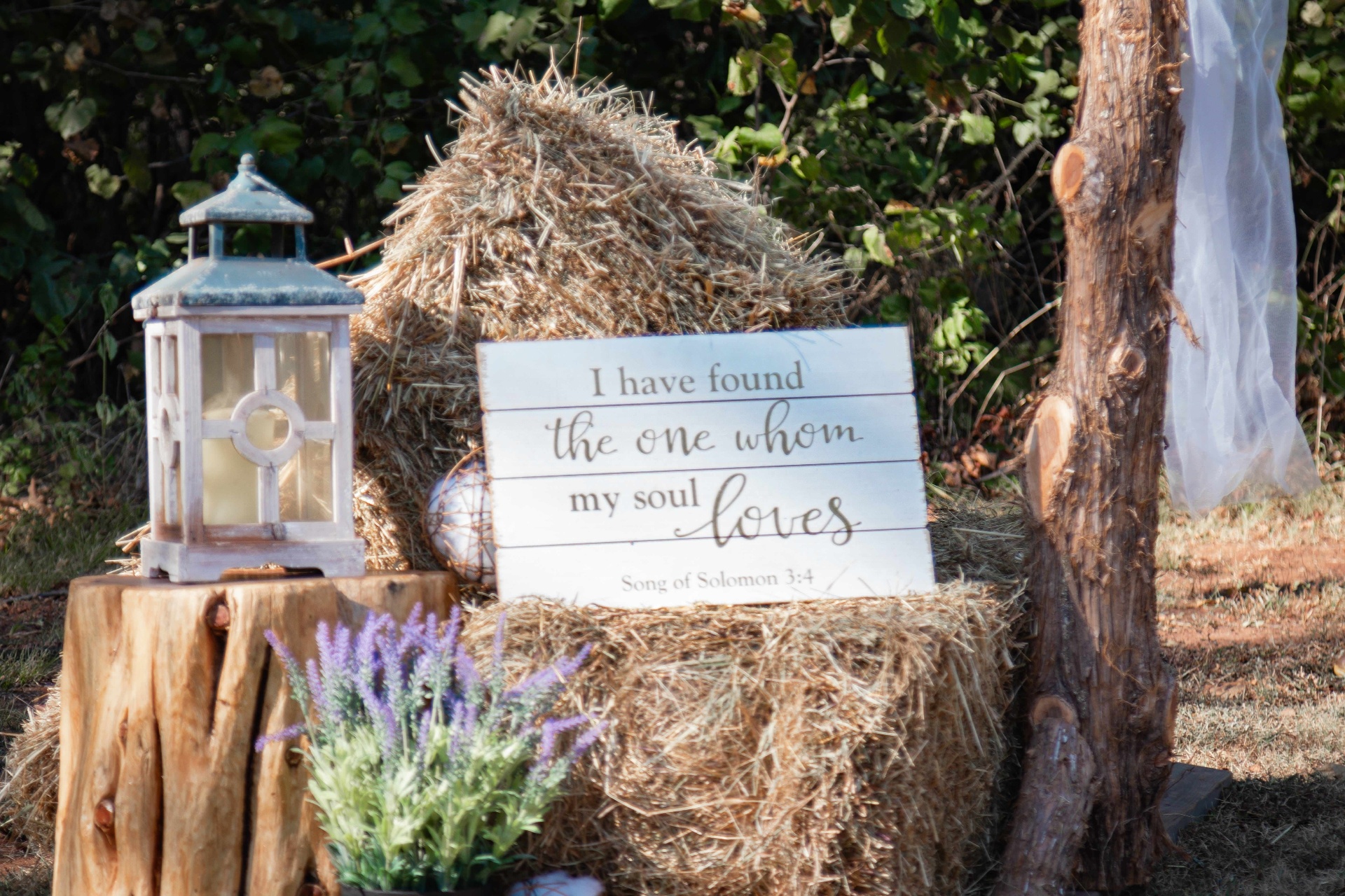 Hand-lettered wooden sign reading 'I have found the one whom my soul loves' on a hay bale with a lantern and lavender
