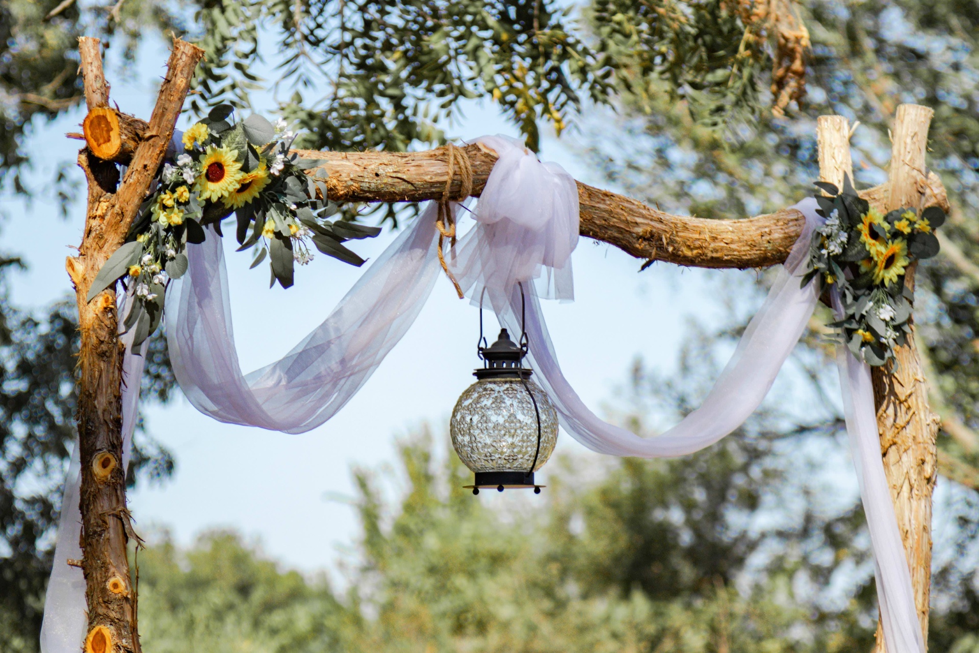 Rustic wooden wedding arch with sunflowers, eucalyptus, sheer lavender drapery, and a hanging lantern